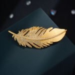 Elegant gold feather brooch wholesale featuring a brushed matte gold vane contrasted with a sparkling micro-pave cubic zirconia lower plume from junejewelry.com