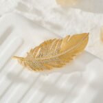 Elegant gold feather brooch wholesale featuring a brushed matte gold vane contrasted with a sparkling micro-pave cubic zirconia lower plume from junejewelry.com