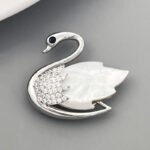 Elegant mother of pearl swan brooch wholesale featuring a carved natural shell wing, pavé cubic zirconia feathers, a black CZ eye, and a magnetic closure from junejewelry.com