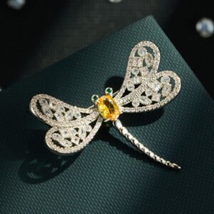 Dragonfly brooch wholesale featuring openwork filigree wings set with clear cubic zirconia, an oval gemstone body, and green CZ eyes from junejewelry.com