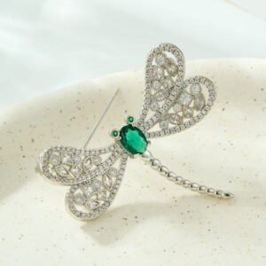 Dragonfly brooch wholesale featuring openwork filigree wings set with clear cubic zirconia, an oval gemstone body, and green CZ eyes from junejewelry.com