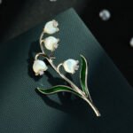 Lily of the valley brooch wholesale featuring carved mother-of-pearl shell bell flowers with cubic zirconia accents and green enamel leaves from junejewelry.com
