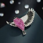 Flying bird crystal brooch wholesale featuring pavé ruby pink cubic zirconia body, clear CZ inner wings, and black enamel feather trim from junejewelry.com