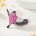 Flying bird crystal brooch wholesale featuring pavé ruby pink cubic zirconia body, clear CZ inner wings, and black enamel feather trim from junejewelry.com