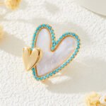 Double heart mother of pearl brooch wholesale featuring a carved shell primary heart with a turquoise or clear CZ halo border alongside a metallic accent heart from junejewelry.com