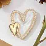 Double heart mother of pearl brooch wholesale featuring a carved shell primary heart with a turquoise or clear CZ halo border alongside a metallic accent heart from junejewelry.com