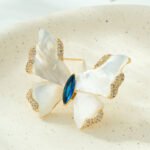 Shell butterfly brooch wholesale featuring iridescent mother-of-pearl wings with cubic zirconia paved edges and a marquise-cut center stone from junejewelry.com