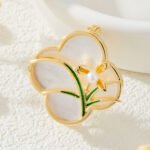 Vintage style four leaf clover mother of pearl orchid brooch wholesale featuring a natural white mother of pearl clover base overlaid with green enamel orchid leaves and a freshwater pearl flower center in gold or silver finish from junejewelry.com