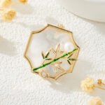 Oriental vintage Chinese style mother of pearl bamboo brooch wholesale featuring a scalloped natural white shell base overlaid with green enamel bamboo stalk, leaves, cubic zirconia accent, and freshwater pearl in gold or silver finish from junejewelry.com