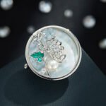 Chinese style enamel chrysanthemum pearl brooch wholesale featuring a circular natural mother of pearl disc, delicate wirework chrysanthemum with green enamel leaf, cubic zirconia sparkles, and a freshwater pearl from junejewelry.com