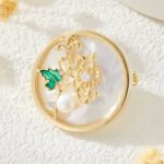Chinese style enamel chrysanthemum pearl brooch wholesale featuring a circular natural mother of pearl disc, delicate wirework chrysanthemum with green enamel leaf, cubic zirconia sparkles, and a freshwater pearl from junejewelry.com