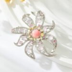 Light luxury pink floral queen conch shell brooch wholesale featuring a pink queen conch shell central cabochon surrounded by yellow, pink, clear cubic zirconia stones, soft purple bead accents, and silver pave openwork petals from junejewelry.com