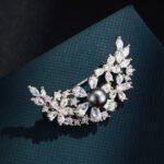 Delicate crescent moon pearl crystal brooch wholesale featuring a sweeping crescent arc encrusted with marquise and pear-cut cubic zirconia floral clusters centered around a smooth pearl accent from junejewelry.com