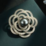 Elegant camellia flower pearl brooch wholesale featuring layered hollow micro-pave cubic zirconia petals centered with a round gray, white, or champagne glass pearl from junejewelry.com
