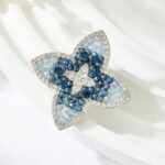Vintage style four petal blue crystal brooch wholesale featuring gradient light and dark blue crystal beads, clear micro-pave CZ outer halo, and a center crystal cross motif from junejewelry.com