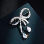Elegant bow knot crystal brooch wholesale featuring a channel-set baguette cubic zirconia ribbon knot with dangling pear-cut CZ teardrop pendants and a convertible back hook from junejewelry.com
