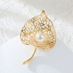 Pearl leaf brooch wholesale featuring a filigree hollow leaf pattern frame with a center glass pearl in gold and silver plating from junejewelry.com