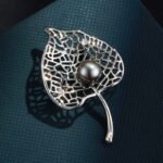 Pearl leaf brooch wholesale featuring a filigree hollow leaf pattern frame with a center glass pearl in gold and silver plating from junejewelry.com