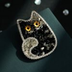 Cute and sparkling black crystal cat brooch wholesale featuring a cat silhouette studded with faceted black resin crystals, micro-pave cubic zirconia border, and vibrant amber eyes from junejewelry.com