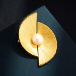 Minimalist brushed gold fan-shaped pearl brooch wholesale featuring dual wire-brushed geometric fan segments, micro-pave cubic zirconia edges, and a center freshwater pearl from junejewelry.com