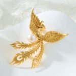 Chinese style brushed golden phoenix pearl brooch wholesale featuring wire-brushed gold feathers, outstretched wings, flowing tail plumes, and a central white freshwater pearl from junejewelry.com.