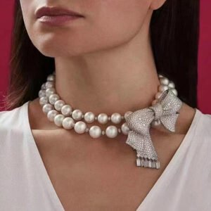 Bow ribbon pearl necklace wholesale featuring double strand round shell pearls, pave cubic zirconia side bow brooch, and baguette crystal drops on palladium plated copper.