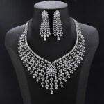 Luxury bridal crystal jewelry set wholesale featuring grand mesh lattice bib collar necklace with starburst flower centerpiece, dangling teardrop tassels, and matching drop earrings on palladium plated copper.