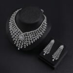 Luxury bridal crystal jewelry set wholesale featuring grand mesh lattice bib collar necklace with starburst flower centerpiece, dangling teardrop tassels, and matching drop earrings on palladium plated copper.