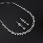 Floral crystal jewelry set wholesale featuring continuous four-petal flower stations necklace with sparkling marquise crystals and matching teardrop dangle earrings on palladium plated copper.