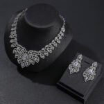 Crown crystal jewelry set wholesale featuring ornate filigree teardrop halo bib collar necklace with large pear cut crystal center and matching chandelier earrings on palladium plated copper base.