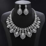 Vintage crystal jewelry set wholesale featuring ornate baroque filigree mesh bib collar necklace with large pear cut center crystals and matching chandelier drop earrings on palladium plated copper base.