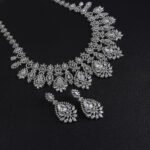 Vintage crystal jewelry set wholesale featuring ornate baroque filigree mesh bib collar necklace with large pear cut center crystals and matching chandelier drop earrings on palladium plated copper base.