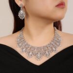 Vintage crystal jewelry set wholesale featuring ornate baroque filigree mesh bib collar necklace with large pear cut center crystals and matching chandelier drop earrings on palladium plated copper base.