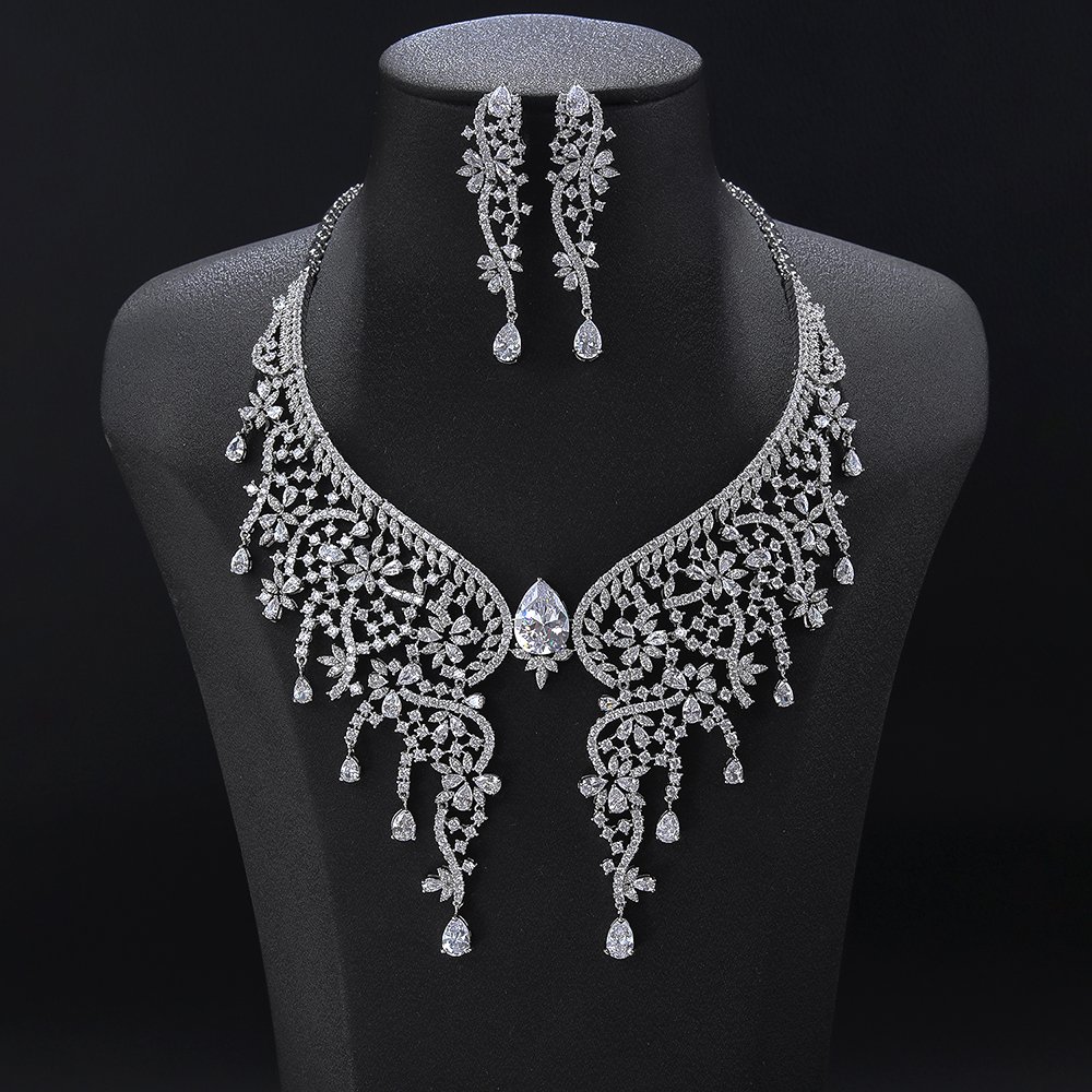 Butterfly wing crystal jewelry set wholesale featuring ornate lace wing collar necklace centered with large pear cut gem, dangling crystal tassels, and matching earrings on palladium plated copper.