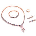 Wholesale crystal drop jewelry set featuring clear round premium crystals, lariat necklace, drop earrings, tennis bracelet, and ring on 18K gold-plated copper base from JuneJewelry.com.