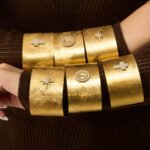Wide brushed 18K gold plated open cuff bangles featuring pavé cubic zirconia north star, cross, and Virgin Mary halo emblems in 316L stainless steel