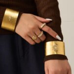Wide brushed 18K gold plated open cuff bangles featuring pavé cubic zirconia north star, cross, and Virgin Mary halo emblems in 316L stainless steel