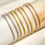 Stacked thin gold, rose gold, and silver stainless steel bangles featuring smooth polished and diamond-cut textured patterns