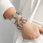 Gold and silver 316L stainless steel open cuff bangles featuring embossed Elizabeth coin medallions and a sculptural wavy cutout design