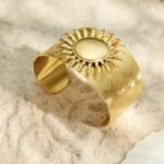 Wide brushed 18K gold plated open cuff bangles featuring dramatic 3D smooth and hammered sunburst emblems in 316L stainless steel