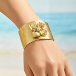 Wide brushed 18K gold plated open cuff bangles featuring a dimensional gold flower with pavé CZ bee accent and a pink enamel blossom